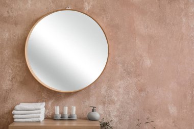 Chest of drawers with towels, candles, soap bottle and mirror hanging on pink wall
