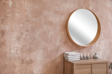 Chest of drawers with towels, candles, soap bottle and mirror hanging on pink wall