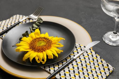 Stylish dinnerware, sunflower and eucalyptus branch on dark table