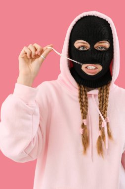 Young woman in balaclava with gum on pink background
