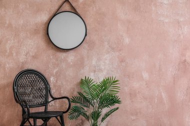Stylish chair, houseplant and mirror hanging on pink wall