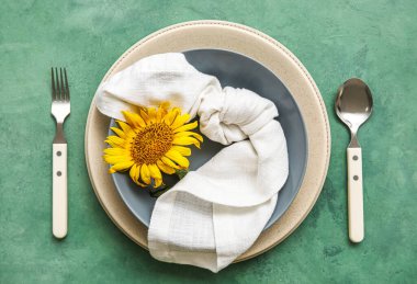 Table setting with sunflower in plate on green background