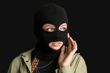 Young woman in balaclava touching face on black background