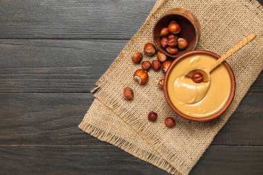 Bowls with tasty hazelnut butter and nuts on dark wooden background