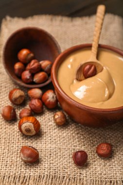 Bowls with tasty hazelnut butter and nuts on table, closeup
