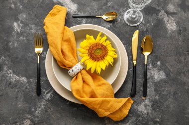Stylish table setting with sunflower in plate on grunge background