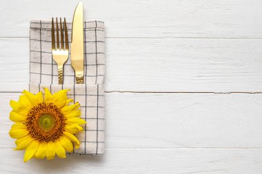 Napkin, cutlery and sunflower on white wooden background