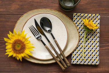 Stylish table setting with cutlery and sunflower on wooden background