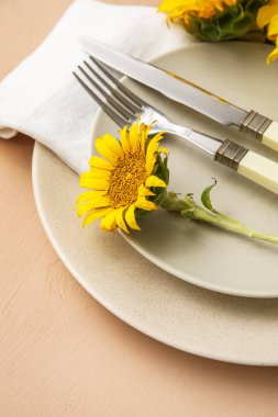 Simple dinnerware and sunflowers on beige table, closeup