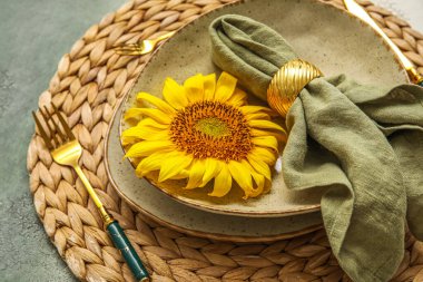 Dinnerware and beautiful sunflower on color table, closeup