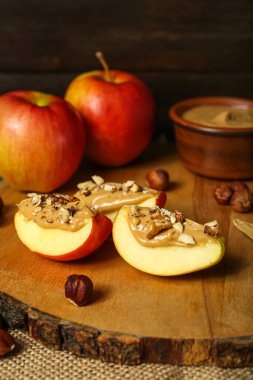 Wooden board of tasty apple wedges with nut butter, closeup