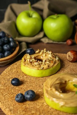 Cork mat of tasty apple rounds with nut butter on wooden table, closeup
