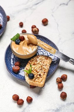 Plate with tasty sandwich, nut butter and hazelnuts on light background