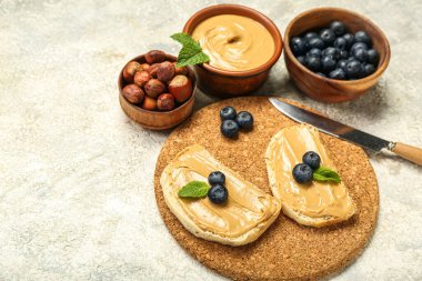 Tasty sandwiches with nut butter, hazelnuts and blueberry on light background