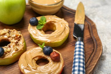 Wooden board of tasty apple rounds with nut butter on table, closeup