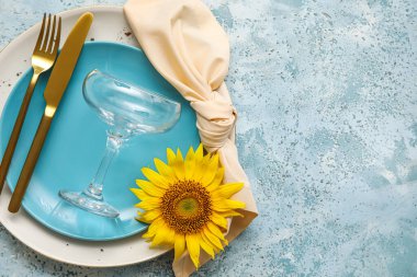 Stylish table setting and sunflower on blue background