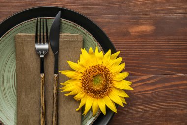 Table setting with stylish cutlery and sunflower on wooden background
