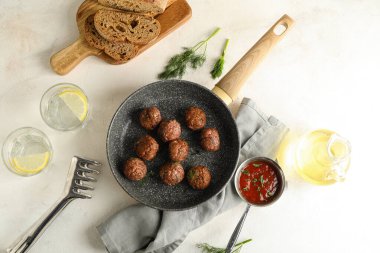 Frying pan with meat balls, bread slices, glasses of water, sauce and oil on white background