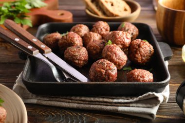 Baking dish with meat balls and cutlery on wooden background, closeup