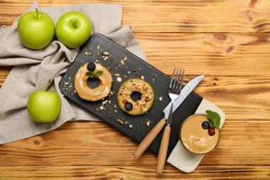 Board of fresh apple rounds with tasty nut butter on wooden background