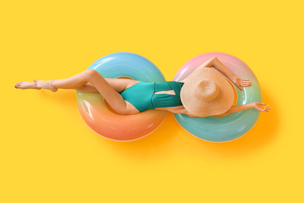 Beautiful young woman in swimsuit and with inflatable rings on yellow background