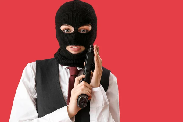 Portrait of young woman in balaclava with gun against red background