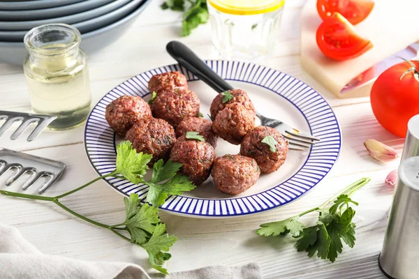 Plate with tasty meat balls, parsley and fork on white wooden background, closeup