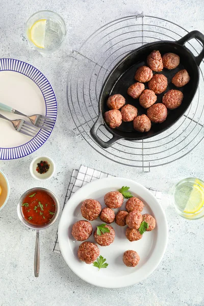 Baking dish with tasty meat balls, plates, glass of water and sauce on grunge background