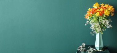 Vase with bouquet of beautiful alstroemeria flowers on table against green background with space for text
