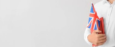 Young male student with UK flag and books on light background with space for text, closeup