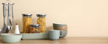 Interior of stylish kitchen with dinnerware, jars of pasta and utensils on counter
