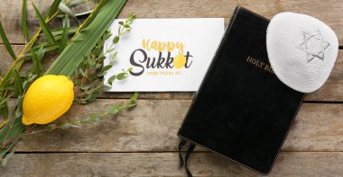 Sukkot festival symbols, greeting card and Bible on wooden background