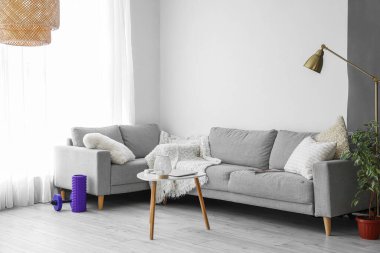Interior of light living room with sofas, foam roller and dumbbell