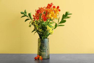 Vase with bouquet of alstroemeria flowers on table near yellow wall