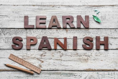 Text LEARN SPANISH, stationery and paper ship on white wooden background