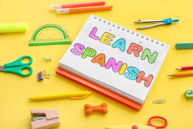 Notebook with text LEARN SPANISH and stationery supplies on yellow background