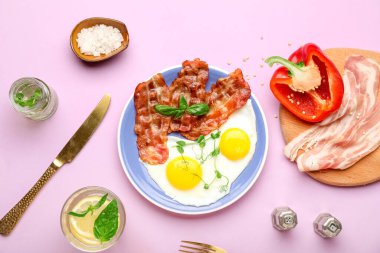 Plate with tasty fried eggs, bacon and ingredients on pink background