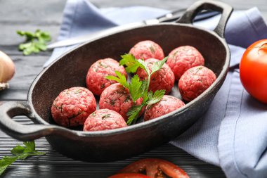 Baking dish with raw meat balls and parsley on dark wooden background, closeup