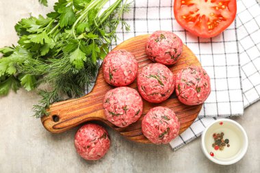 Cutting board with raw meat balls, herbs, tomato and napkin on grunge background