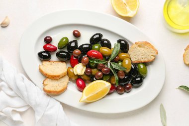 Plate with different olives, bread and lemon on light background