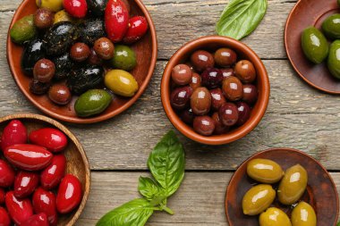 Bowls and plates with different kinds of delicious olives on wooden background, closeup