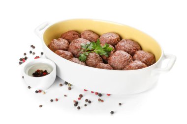 Baking dish with tasty meat balls, parsley and peppercorns on white background