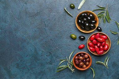 Composition with bowls of different olives and green leaves on dark color background