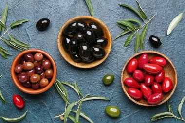 Composition with bowls of different olives and green leaves on dark color background