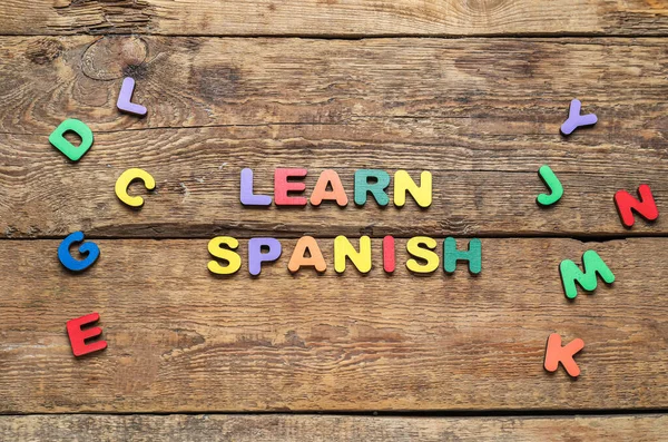 Text LEARN SPANISH and letters on wooden background