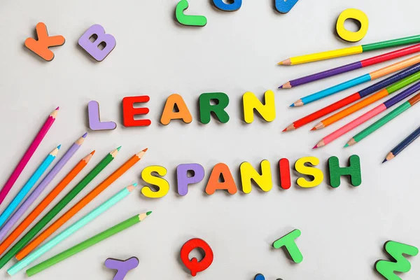 Text LEARN SPANISH with letters and pencils on grey background