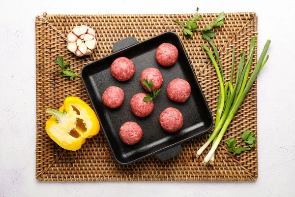 Wicker mat with baking dish, raw meat balls and vegetables on white background