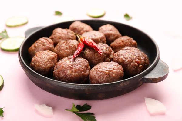 Baking dish with tasty meat balls and vegetables on pink background