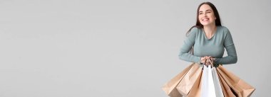 Happy young woman with shopping bags on grey background with space for text