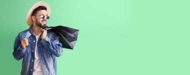 Handsome man with credit card and shopping bags on green background with space for text
